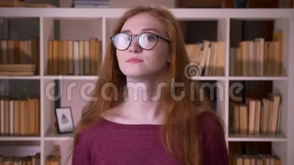年轻的红头发迷人的白种人戴着眼镜的女学生一边打招呼一边微笑地看着镜头视频的预览图