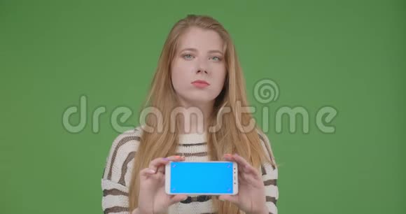 用手机拍摄年轻漂亮的白种人女性的特写镜头并显示蓝色的彩色屏幕来拍摄它视频的预览图