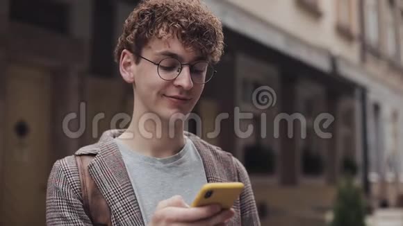 年轻的红色卷发千禧年在眼镜聊天和短信智能手机使用消息应用程序滚动他的视频的预览图