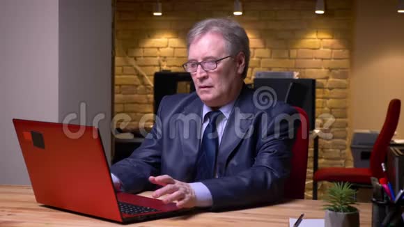 戴眼镜和穿着正式服装的老人在办公室里用笔记本电脑工作时生气和恼怒的肖像视频的预览图