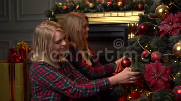 两个穿红色衬衫的金发女郎为新年或圣诞节装饰圣诞树视频的预览图