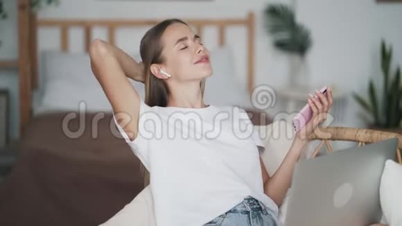 年轻女子用无线耳机听音乐在家跳舞视频的预览图