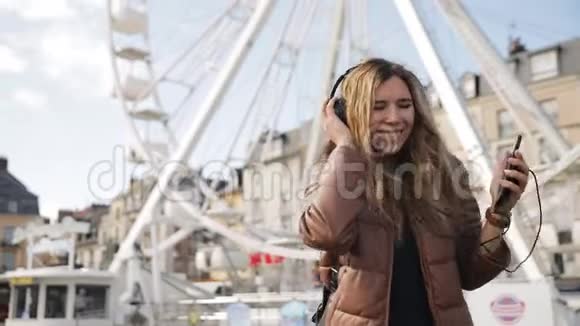 非常漂亮漂亮的年轻女孩女人在摩天轮的背景下用耳机听音乐视频的预览图