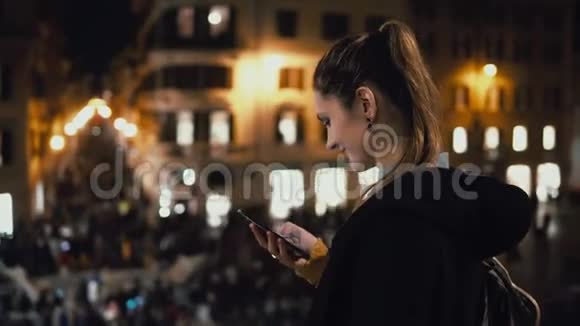 快乐的年轻女人站在人群中使用智能手机晚上和朋友散步聊天的女孩视频的预览图