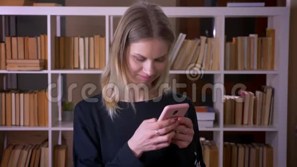 特写镜头年轻迷人的女学生在手机上发短信看着镜头兴高采烈地在室内视频的预览图