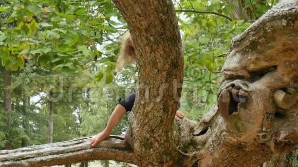 可爱的小女孩蓝眼睛金发赤脚躲在公园大树的树枝后面视频的预览图