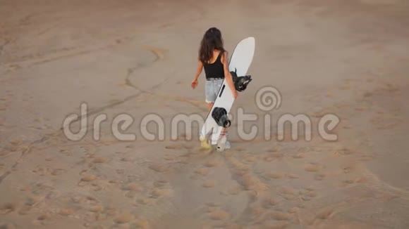 年轻的女孩子走过沙漠手里拿着一块滑雪板转身看着沙漠视频的预览图