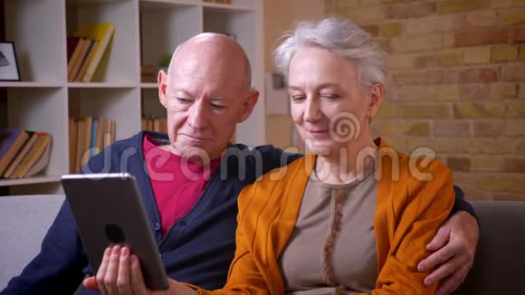 年长的白种人配偶观看平板电脑并讨论它是积极和高兴的沙发在客厅视频的预览图