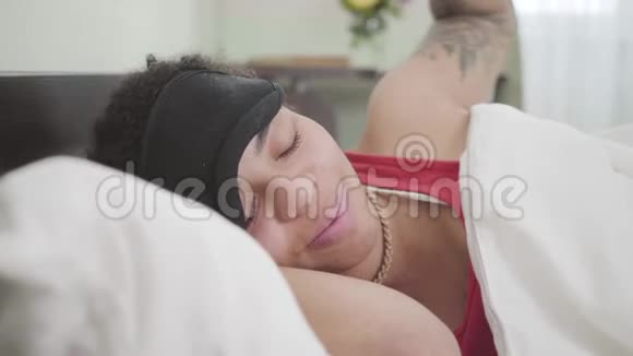 近距离观看可爱的非裔美国妇女躺在白色毯子下与黑色睡眠面具可爱的女孩休息视频的预览图