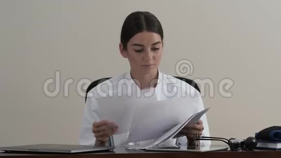 年轻职业女医生坐在办公室的一张桌子旁看报纸的肖像概念视频的预览图