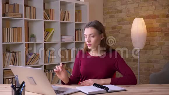 年轻的黑发女商人用笔记本电脑做笔记集中在办公室视频的预览图