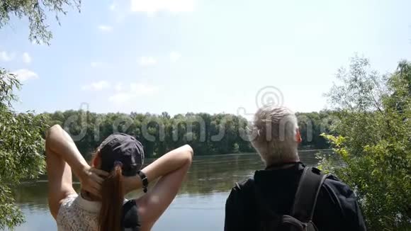 快乐旅行的概念男人和女孩一起远足带背包的徒步旅行者停在河岸上放松他们是视频的预览图
