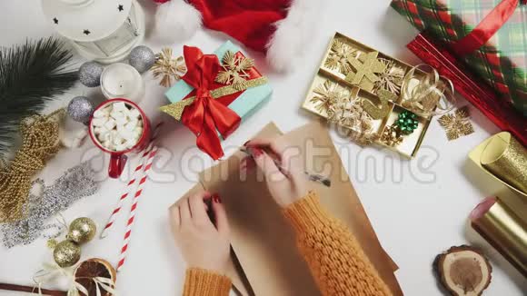 女性手在木桌上写礼物清单有礼物包装纸红色圣诞装饰品视频的预览图