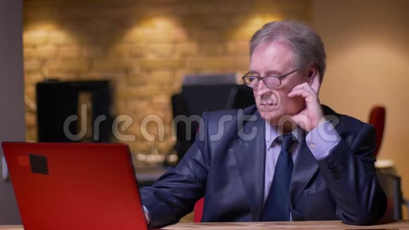 一幅高级商人穿着正式服装手上拿着笔记本电脑在办公室里疲惫不堪视频的预览图