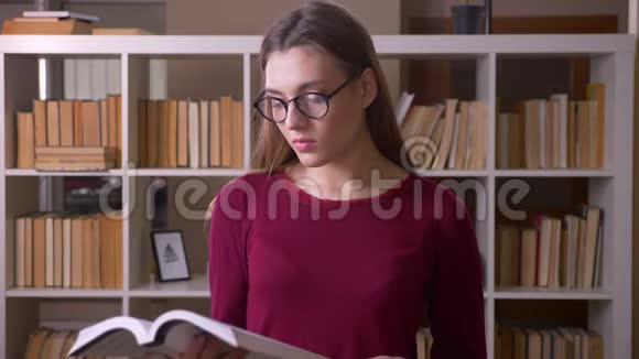 年轻漂亮的黑发女学生戴着眼镜在图书馆专心看书视频的预览图