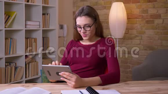 年轻漂亮的黑发女商人戴着眼镜在平板电脑上玩游戏在办公室里很开心视频的预览图