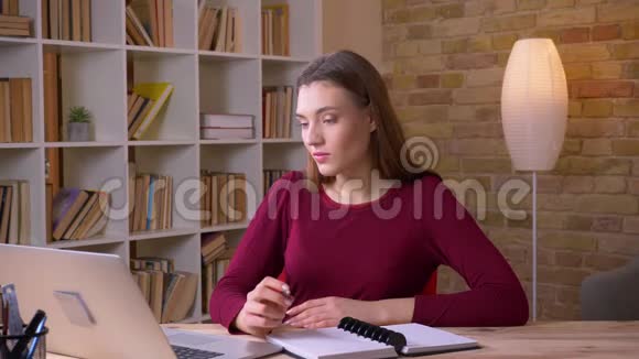 年轻的黑发女商人在办公室里用笔记本电脑和笔记本电脑对着镜头微笑视频的预览图