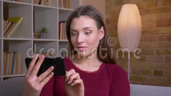 年轻快乐的黑发女性展示直立的水平绿色手机屏幕推荐应用在家里视频的预览图