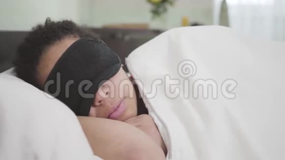 美籍非裔妇女睡在白色毯子下黑色睡眠面具的特写镜头疲倦的女孩视频的预览图
