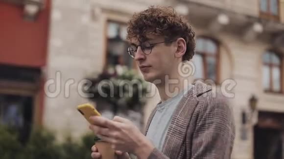 眼镜中年轻貌美的学生穿着带支票的夹克四处乱跑看着他的智能手机视频的预览图