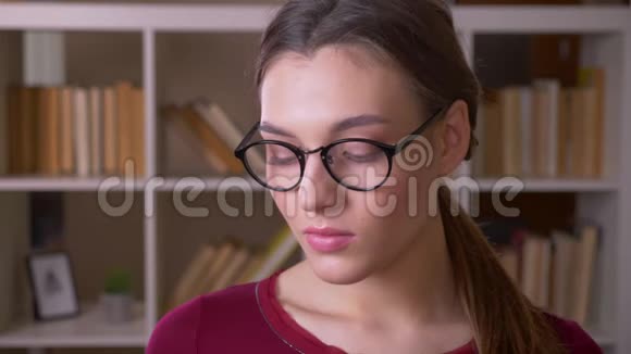年轻的黑发女学生带着马尾辫戴着眼镜的肖像微笑着在图书馆里调情视频的预览图