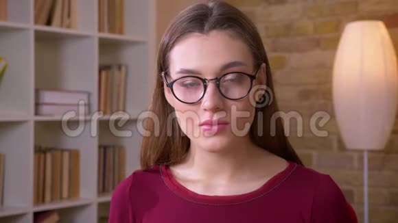一幅美丽的黑发长发女学生戴着眼镜的特写肖像平静而固定地在镜头中观看视频的预览图