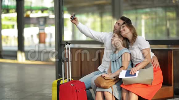 假期时间岩石微笑美丽的家庭在机场或机场等待航班时用智能手机自拍视频的预览图