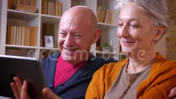 在舒适的家里一对老白种人夫妇在平板电脑上和他们的朋友一起玩网络视频游戏视频的预览图