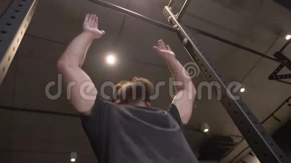 成年人肌肉发达的运动员在健身房里跳着把自己抬到酒吧里的特写镜头视频的预览图