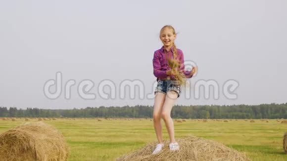 嬉戏的女孩在干草堆上跳舞手里拿着稻草在收割庄稼快乐的少年女孩在大海捞针视频的预览图