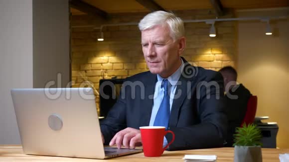 老白种人办公室工作人员使用笔记本电脑和在工作场所的办公室内喝咖啡的特写镜头视频的预览图