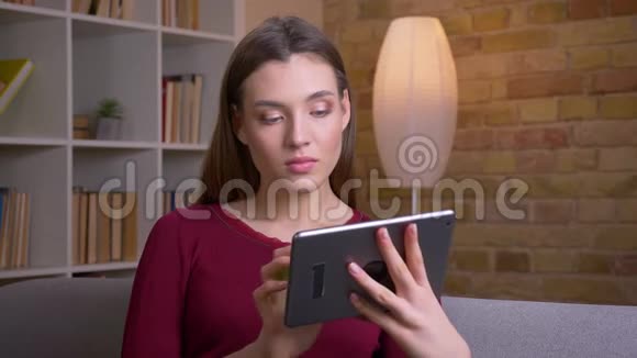 年轻美丽的黑发女性展示水平绿色屏幕的平板电脑进入相机推荐应用程序在家里视频的预览图