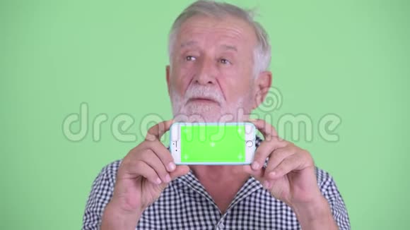 一脸快乐的大胡子男人一边看手机一边思考视频的预览图