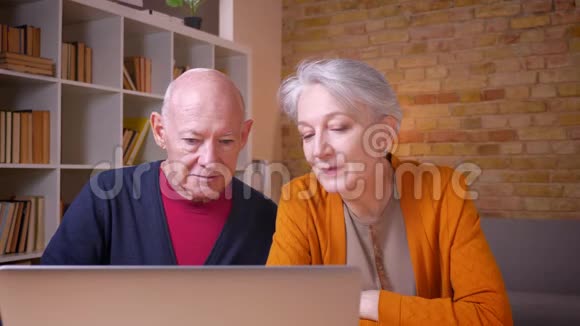 年长的白发白种人夫妇在办公室评论笔记本电脑的内容视频的预览图