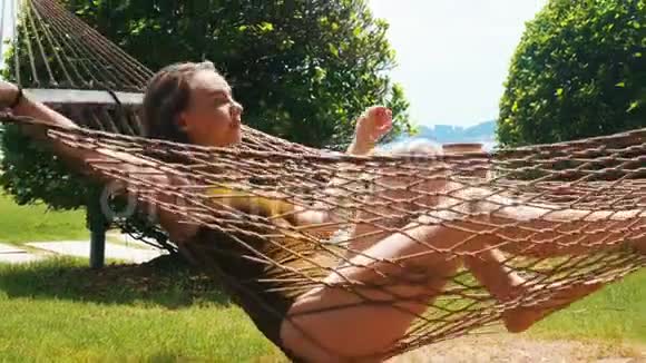 一位身穿泳衣躺在吊床上享受假期的年轻美女视频的预览图