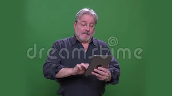 戴着眼镜的美国资深灰发男子在标签上的视频聊天被隔离在绿色的彩色背景上视频的预览图