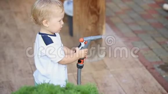 可爱可爱的白种人金发幼儿男孩玩着帮助父母用软管和喷头给花园和草坪浇水视频的预览图