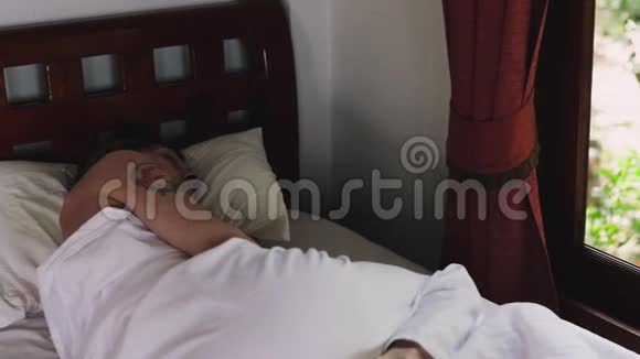 一个人睡在酒店房间里俯瞰花园在旅馆里睡在白色毯子下的男人视频的预览图