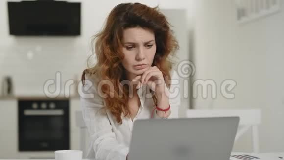 沮丧的女人在家工作电脑年轻女士盯着厨房的笔记本电脑视频的预览图