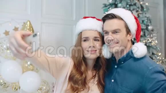 圣诞树附近圣诞老人帽子里的笑脸情侣自拍的肖像视频的预览图