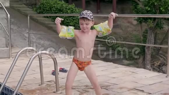 穿着袖子和帽子的小男孩在度假时跳进游泳池男孩在热带的游泳池里游泳儿童潜水视频的预览图