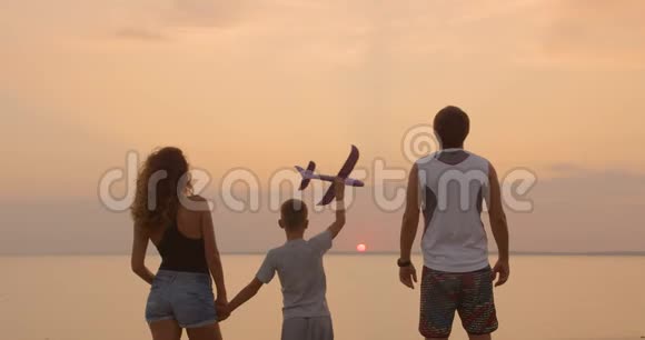 一个幸福的家庭那个男孩和他的父亲和母亲在日落时带着玩具飞机视频的预览图