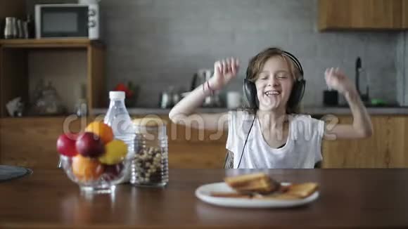 可爱的女孩戴着现代耳机在餐桌上跳舞视频的预览图