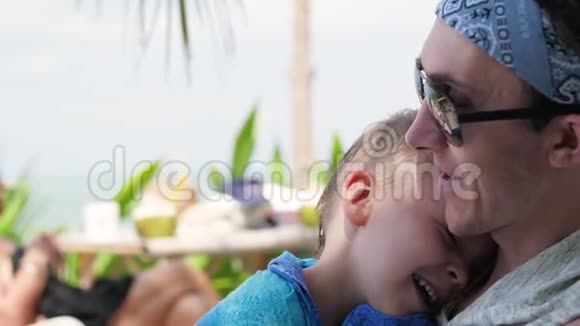 父子二人正相对而坐亲密无间父亲正和儿子坐在海滩上度假视频的预览图
