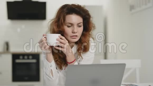 专注的女人在开放式厨房工作笔记本电脑年轻女士喝咖啡视频的预览图