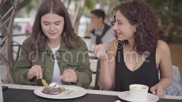 两个女朋友坐在户外咖啡馆吃蛋糕的肖像女人用美味的甜点招待女朋友视频的预览图