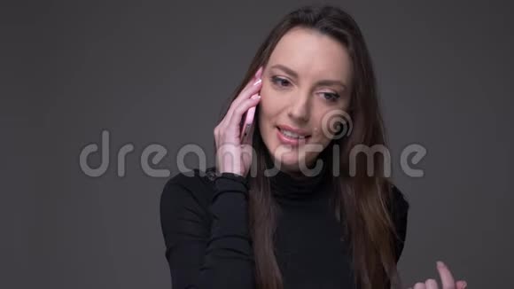 有魅力的黑发女人在手机上交谈的肖像在灰色背景下是快乐和积极的孤立视频的预览图