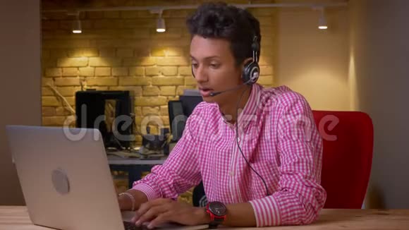 印度年轻商人在办公室室内用耳机打字的特写镜头视频的预览图