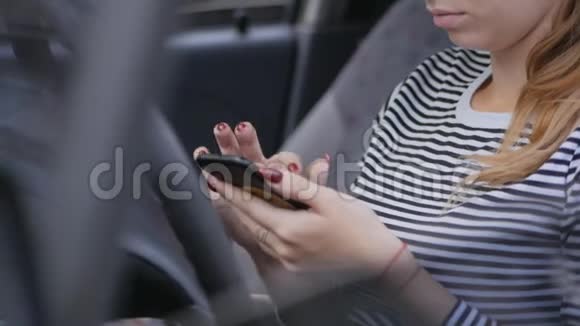 年轻的女人戴着眼镜坐在车轮后面在智能手机上打字视频的预览图