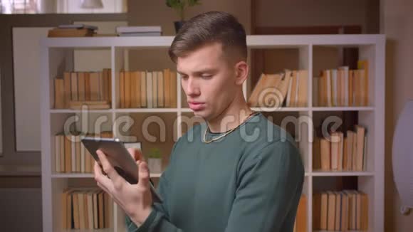 一幅年轻的男学生专心看平板电脑对图书馆很感兴趣视频的预览图